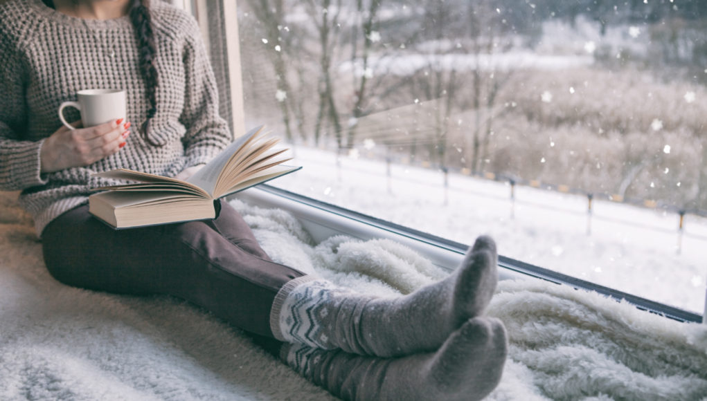 kobieta siedząca przy oknie i czytająca książkę zimą
