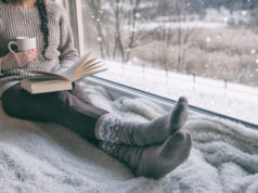 Świetne pozycje książkowe na chłodne, jesienne wieczory – małe zestawienie kobieta siedząca przy oknie i czytająca książkę zimą