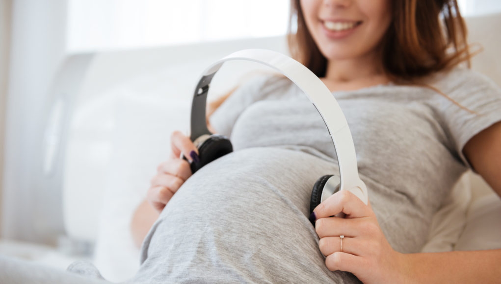 Kobieta w ciąży przykładająca słuchawki do brzucha