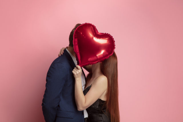 zakochana para całująca się za balonikiem w kształcie serca