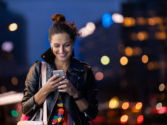 Przeniesienie numeru do innej sieci: co trzeba zrobić, aby nasz numer został poprawnie przeniesiony do innego operatora? młoda dziewczyna ze smartfonem w ręku na tle miasta wieczorem