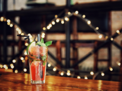 Domowy barek – jak go wyposażyć? drink w szklance na drewnianym stole w tle lampki