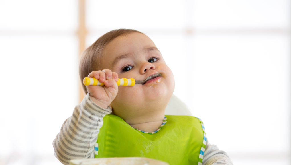 niemowlę jedzące łyżeczką posiłek z miski