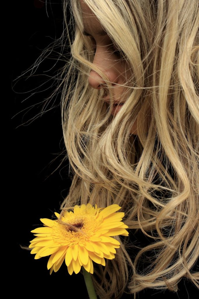 kobieta z pięknymi włosami trzymająca w ręku żółty kwiatek