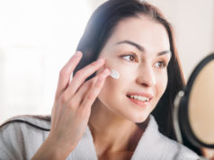 Codzienna pielęgnacja twarzy – jak powinna przebiegać? kobieta przed lustrem nakładająca krem na twarz