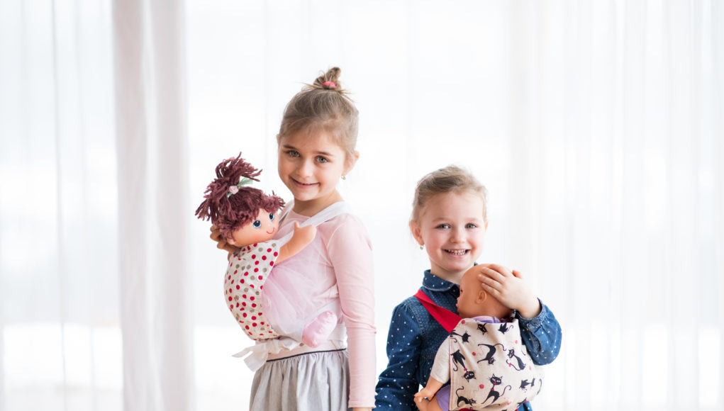 dwie dziewczynki noszące lalki w nosidełkach