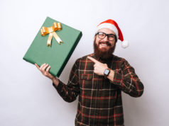 Najciekawsze prezenty technologiczne pod choinkę mężczyzna z brodą w czapce mikołaja i prezentem w dłoni
